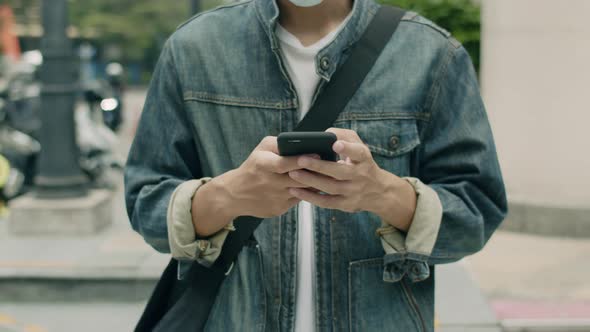 Asian man wearing a surgical mask and using a smartphone.