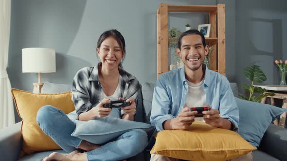 Happy asia young couple man and woman sit on couch use joystick controller play video game.