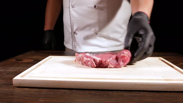 A Cook in a White Apron Puts a Piece of Raw Meat on a Wooden Board, Salt, Season