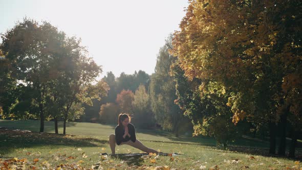 Young Woman Doing Exercises and Stretching in Autumn City Park on a Yoga Mat