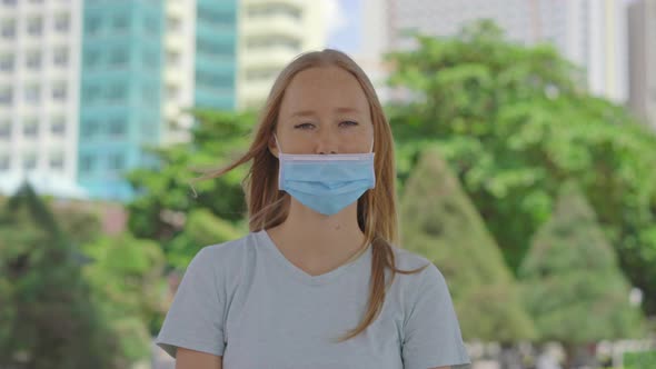 A Young Woman Stands on a Street. She Is Wearing Medical Face Mask in the Wrong Way alt