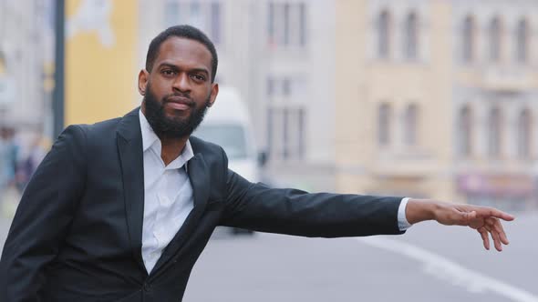 Young Black Bearded Businessman Standing on Sidewalk Outdoors Waving Hand Signaling to Driver Stop alt