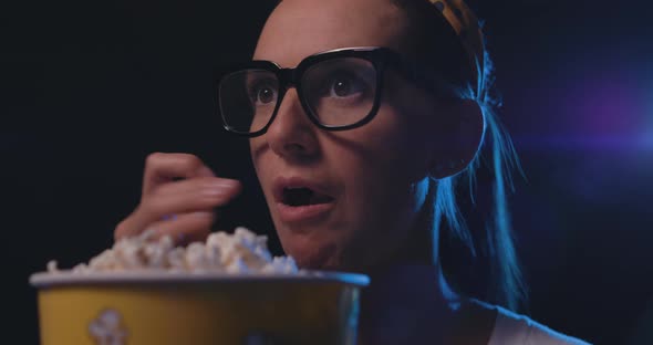 Woman watching a thriller movie and eating popcorn at the cinema