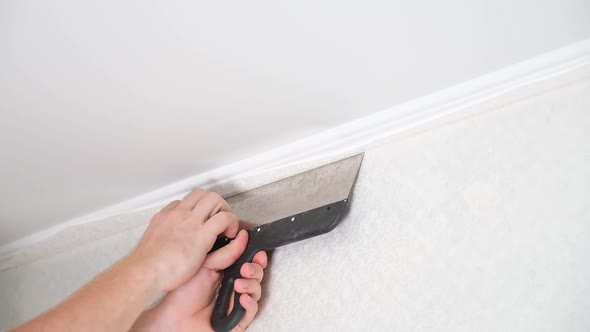Man Cuts Wallpaper Near Ceiling Moldings Using Box Cutter and Putty Blade