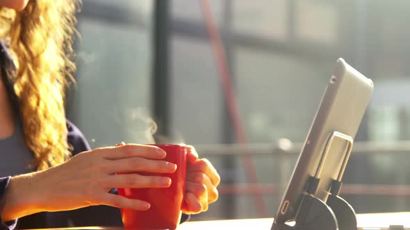Female executive using digital tablet and mobile phone while having coffee alt