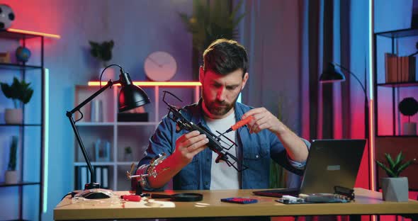 Man Sitting at the Table at Home in the Evening and Compose All Elements of Drone Using screwdriwer alt