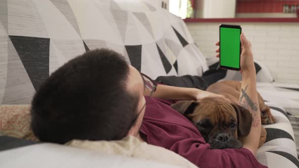 young man with his dog lying on the couch staring at his cell phone, green screen alt