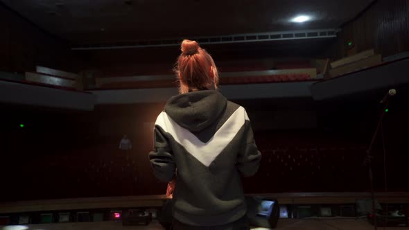 Back View of Female Singer Singing and Dancing on Big Concert Hall Stage with Empty Auditorium alt