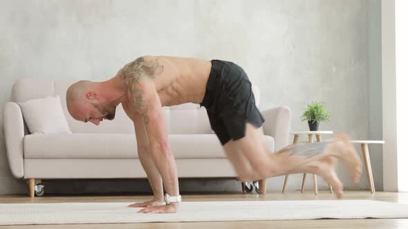 Athletic Man in Shorts Is Training and Doing Dynamic Exercises in Plank at Home