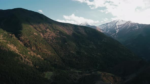 Drone flies over mountain valley, autumn sunset time, snowy summits on background, cloudy sky