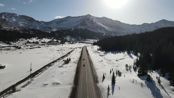 4k drone video of cars driving down road in winter in the Rocky Mountains in Colorado. alt