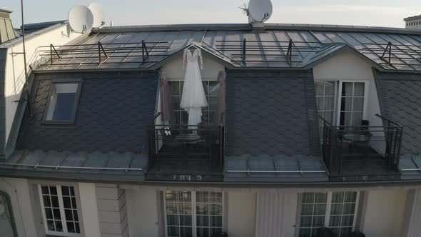 Wedding Gown Dress Hanging at Balcony Terrace Doorway Waits for Bride at Sunny Morning Aerial View alt