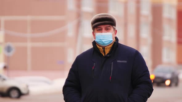 Closeup of a Man in a Medical Mask Stands and Looks Forward and Around alt