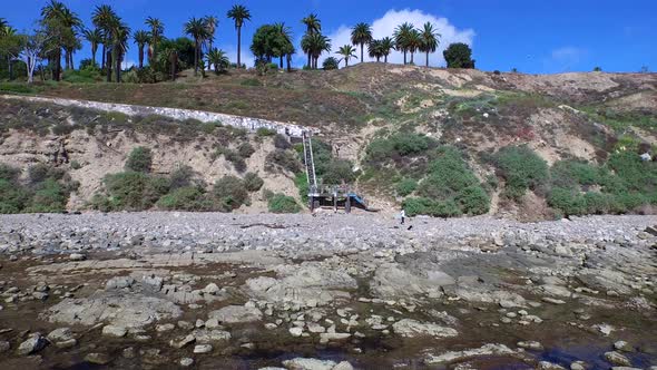 Aerial shot of a young man running stairs on the side of a cliff by the ocean. alt