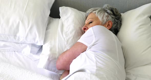 Senior woman sleeping on bed in bedroom alt