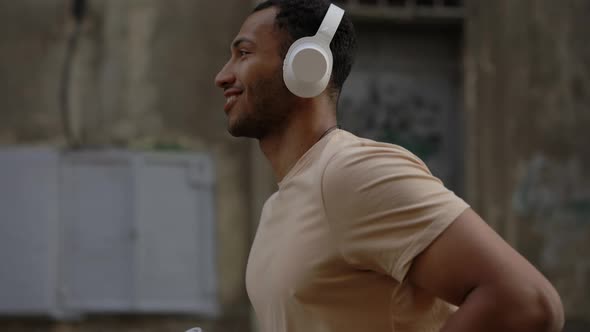 Side Close View of the Smiled African American Man Running and Wearing Headphones in the Old City alt
