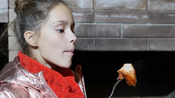 Cute Teenage Girl in a Jacket and a Scarf Beautifully Eats Meat with a Fork
