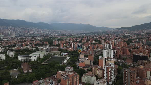 Flying forward, Aerial view of large colorful city and soccer field, Medellin, Colombia alt