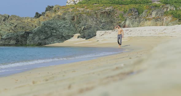 The Handsome Man with a Perfect Athletic Body in Gray Trousers Having Fun on a Deserted Beach in the alt