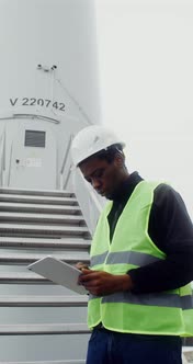 A Man in a Work Uniform is Diagnosing a Wind Turbine Using a Digital Tablet alt
