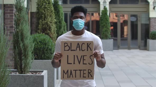African American Man in a Medical Mask Holding a Poster with the Inscription Black Lives Matter alt