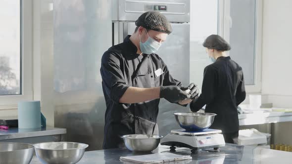 Professional Male Cook in Uniform and Covid Face Mask Beating Eggs in Slow Motion As Woman Working alt