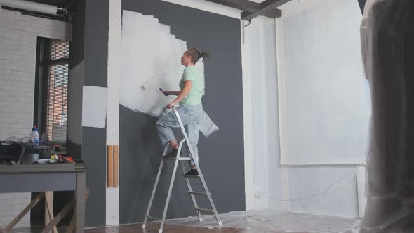 stylish designer or painter sings and dances while painting walls with paint roller in room  alt