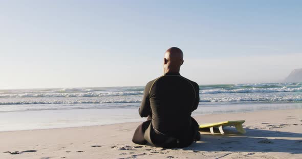 Senior african american man sitting with a surfboard at the beach alt