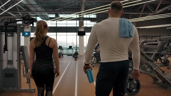 Couple of Athletes Go Through the Gym to the Exercise Machines alt