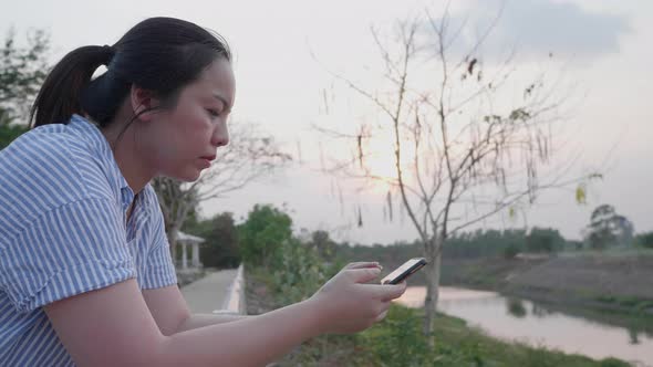 Asian woman chatting in smartphone to friend at outdoor landscape river alt