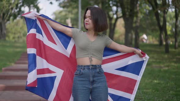 Medium Shot of Confident Smiling Little Person Stretching Hands with British Flag Standing in Park alt