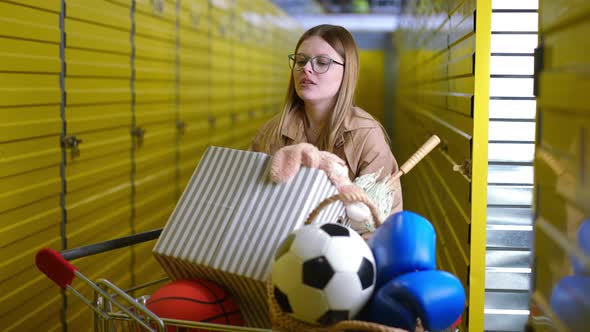 Sad Tired Woman in Eyeglasses Putting Box with Personal Belongings on Trolley Rubbing Forehead alt