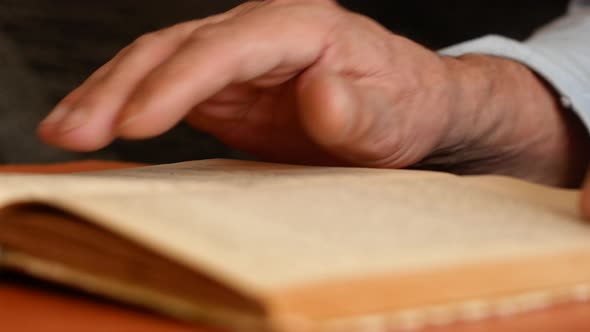 Close-up of an open old book in the hands of an elderly man. alt