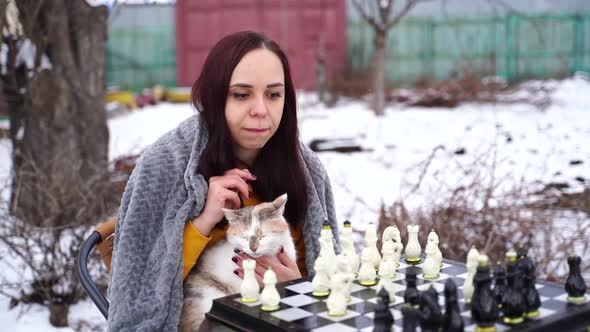 Young Woman Sitting with Cat and Playing Chess in Yard alt