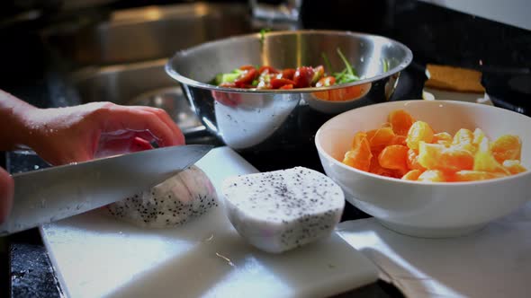 Woman Cuts Dragon Fruit for Fruit Salad on a White Plastic Board in the Kitchen alt