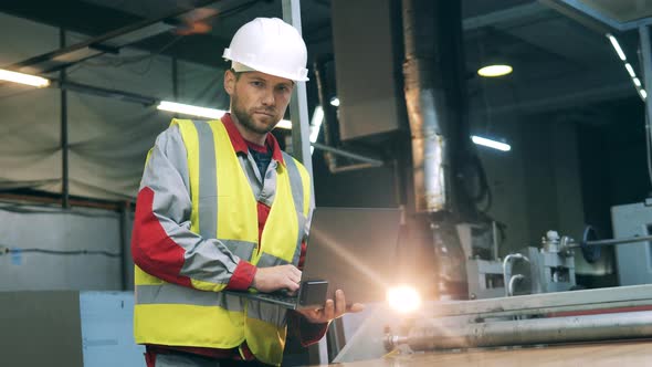 Worker in Uniform and Helmet Typing on Laptop at Metal Working Factory alt