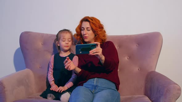 Millennial mother taking a selfie with her daughter on the couch.