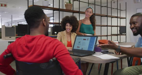 Diverse male and female business colleagues and disabled businessman talking and using laptop alt