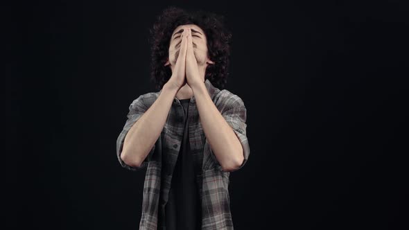 The Charismatic Young Man Impatient Prays with His Eyes Closed and Crosses His Fingers for Good Luck alt