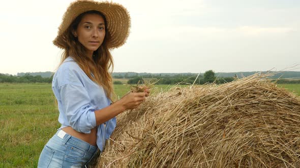 Pretty Young Woman Stands Near Haystack and Plays With Straw