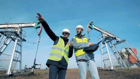 Oil Extraction Site with Two Workers Having a Conversation. Working Oil Pumps, Oil Rigs on a alt