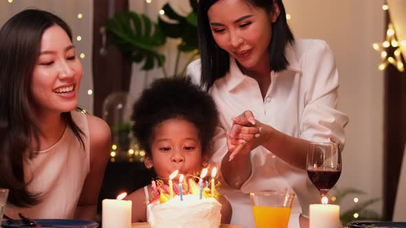 Happy little girl celebrating her birthday with Lgbt family blowing out the candles alt