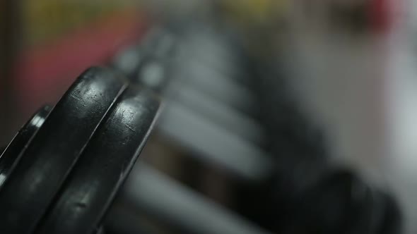 Rack focus shot of dumbbells lying on shelf ready for workout, gym atmosphere alt