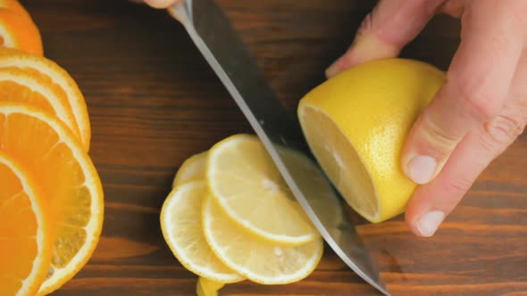 Male hand with big knife slicing lemon citrus fruit on the cutting board at kitchen