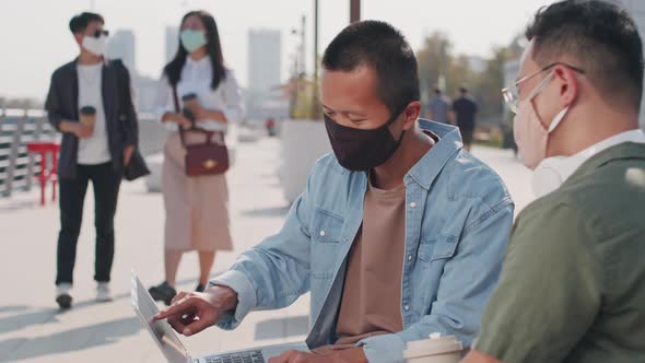 Two Asian Men Discussing Presentation on Laptop Outdoors alt