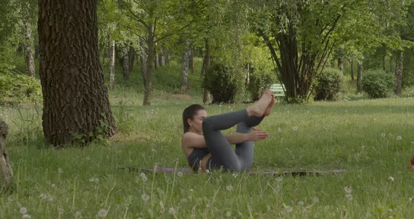Young Girl in Sports Suit in the Park on a Lawn Doing Exercises Doing Fitness Yoga alt