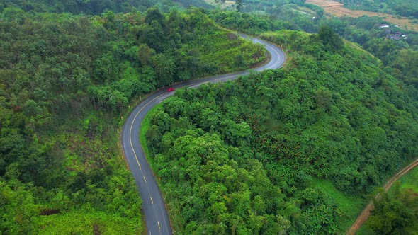 Aerial view over a winding road in the mountains of a tropical forest, Thailand. alt