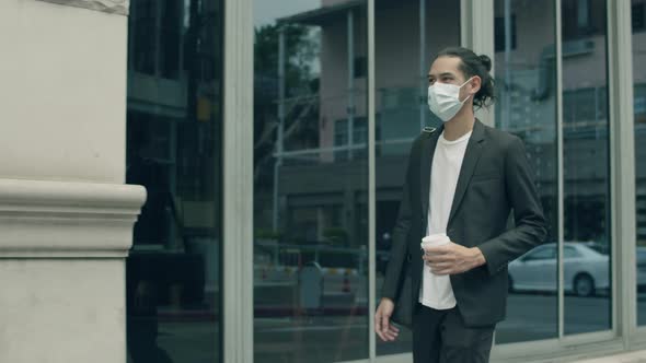 Asian businessman casual dress wearing a mask holding coffee cup.