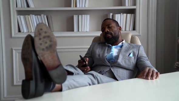 African-American Bearded Man in a Gray Suit and Shirt. A Businessman Is Sitting in a Bright Office alt