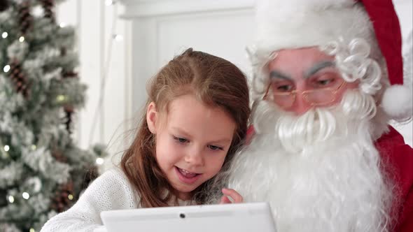 Happy Little Girl Showing Surprised Santa Presents on the Tablet alt